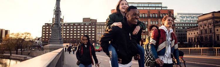En grupp glada ungdomar går över en bro i stadsmiljö
