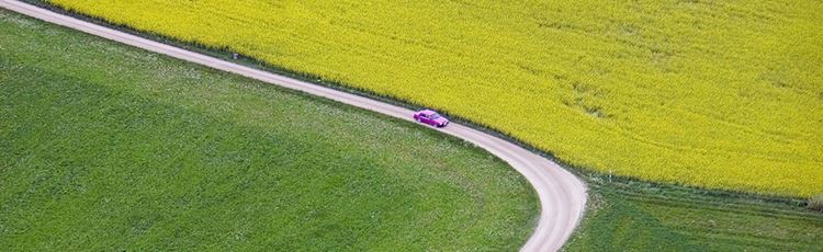 Flygfoto av en bil på en väg som slingrar sig genom gula och gröna fält.